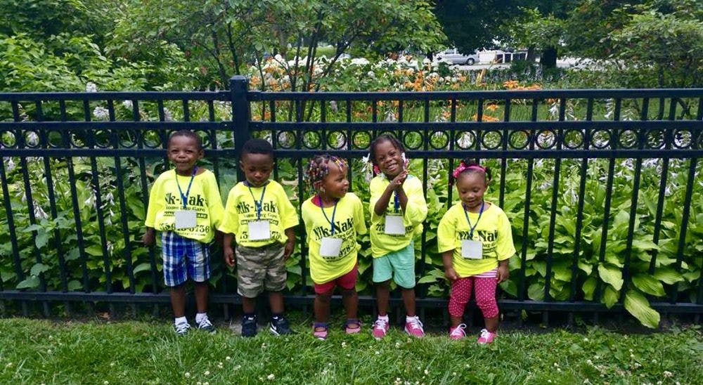 Five children in yellow shirts standing in front of a fence