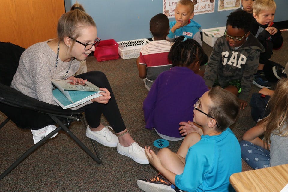 Person reading to a group of children in a classroom