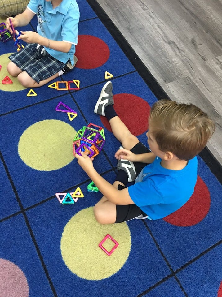 Two children playing with magnetic building toys on a patterned rug