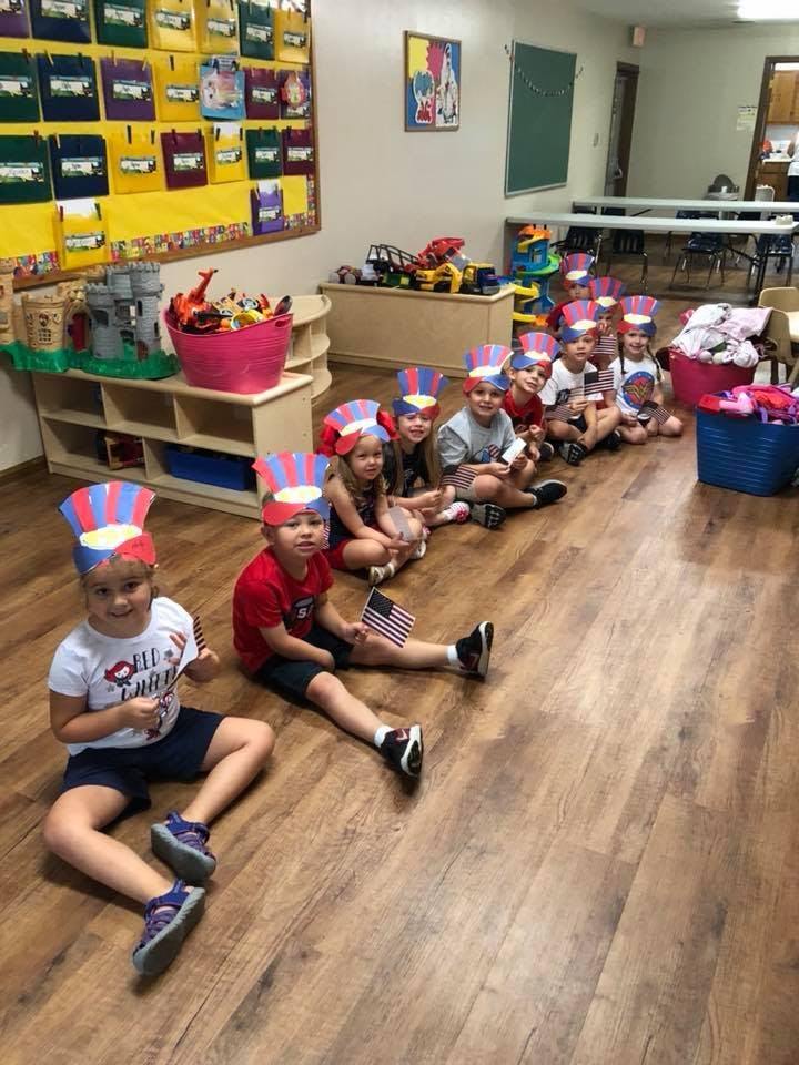 Children in patriotic hats sitting on the floor in a classroom