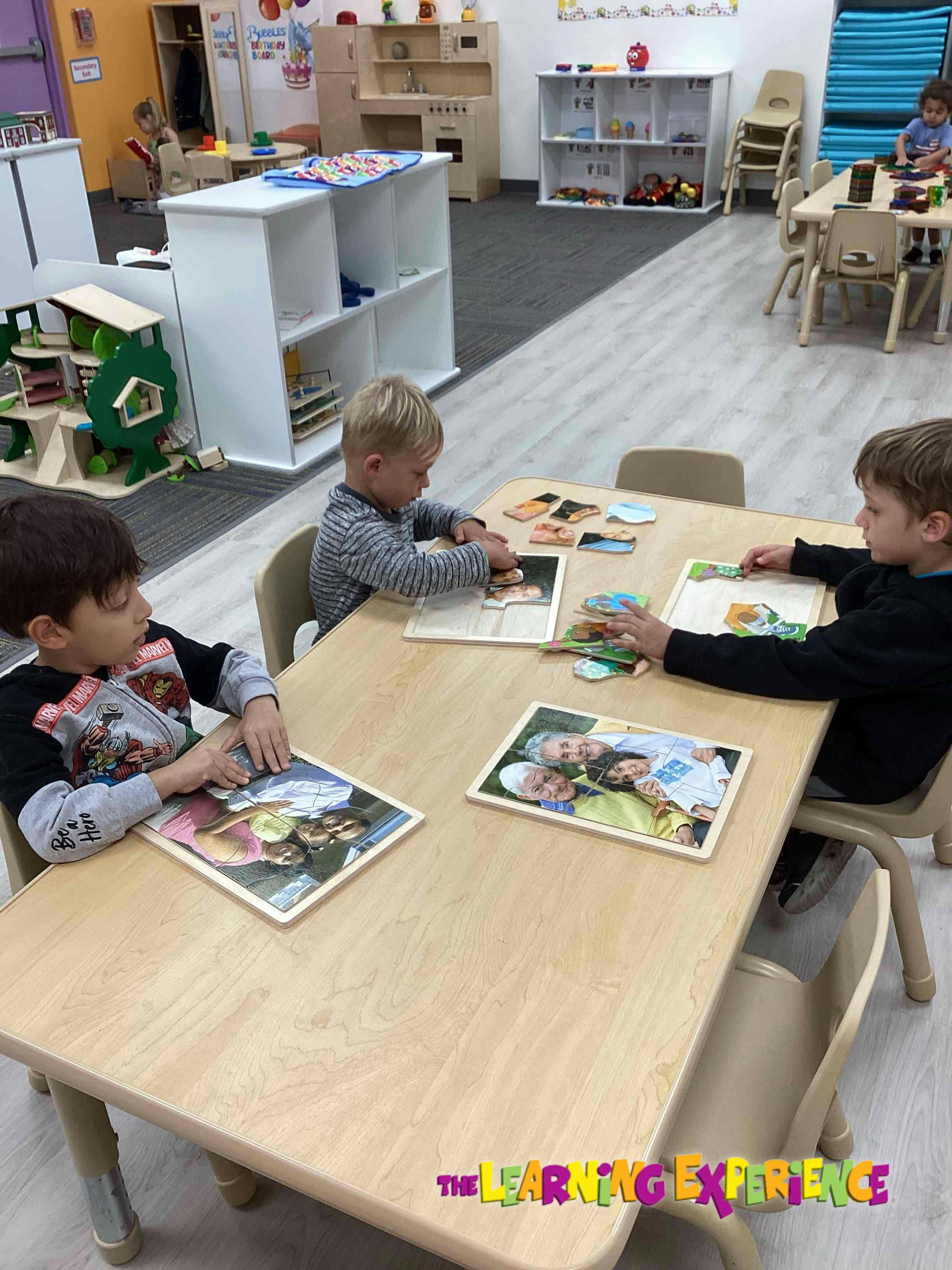 Three children at a table working on puzzles in a classroom