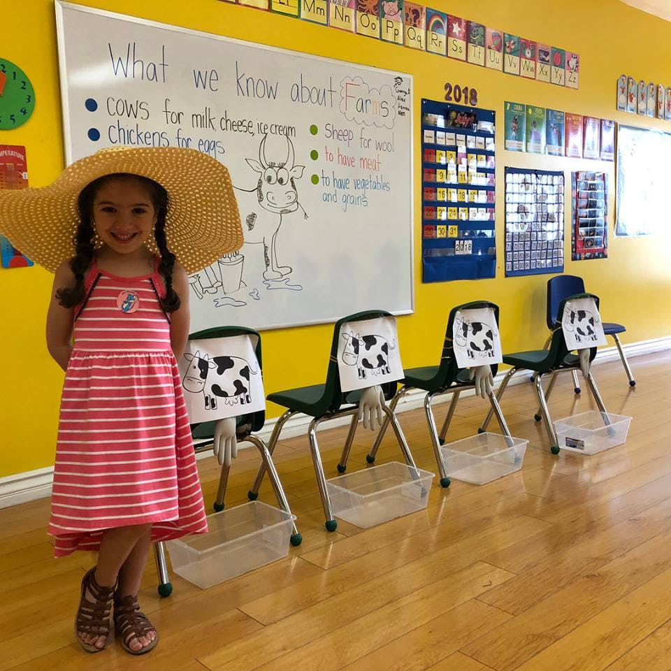 Child in a large straw hat and striped dress standing in a classroom