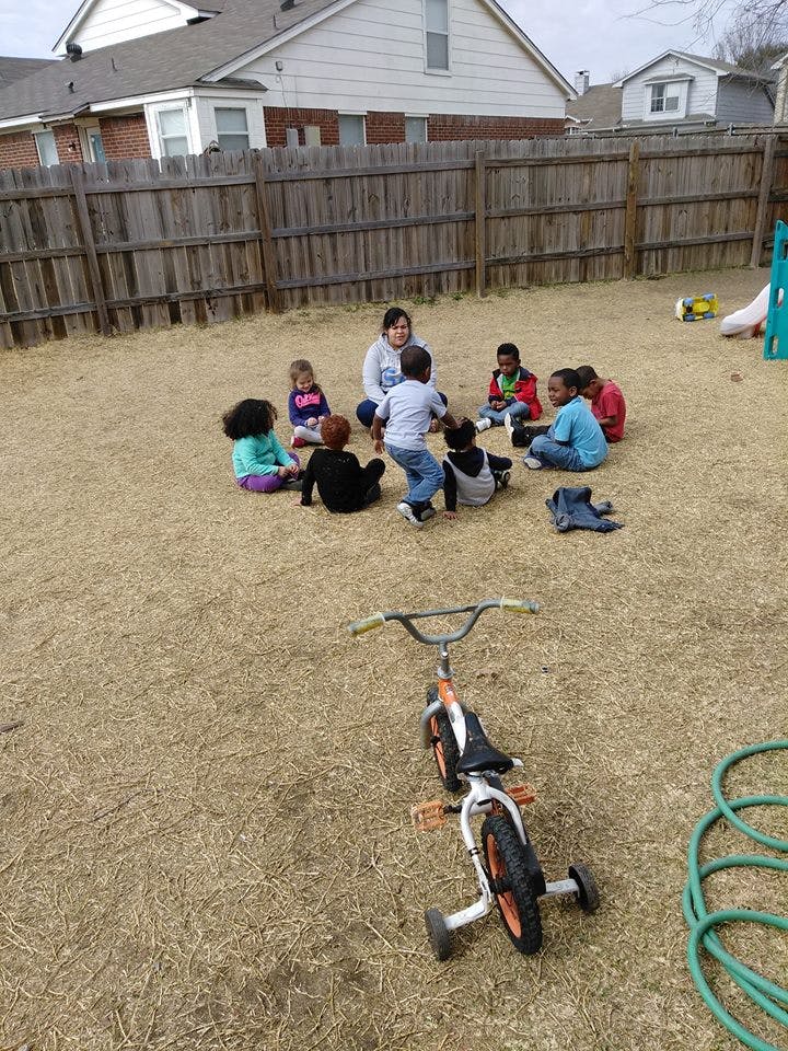 Person and children sitting in a circle on dry grass