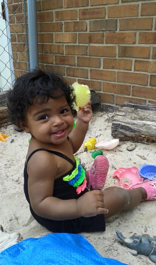 Child sitting in sand holding a yellow toy