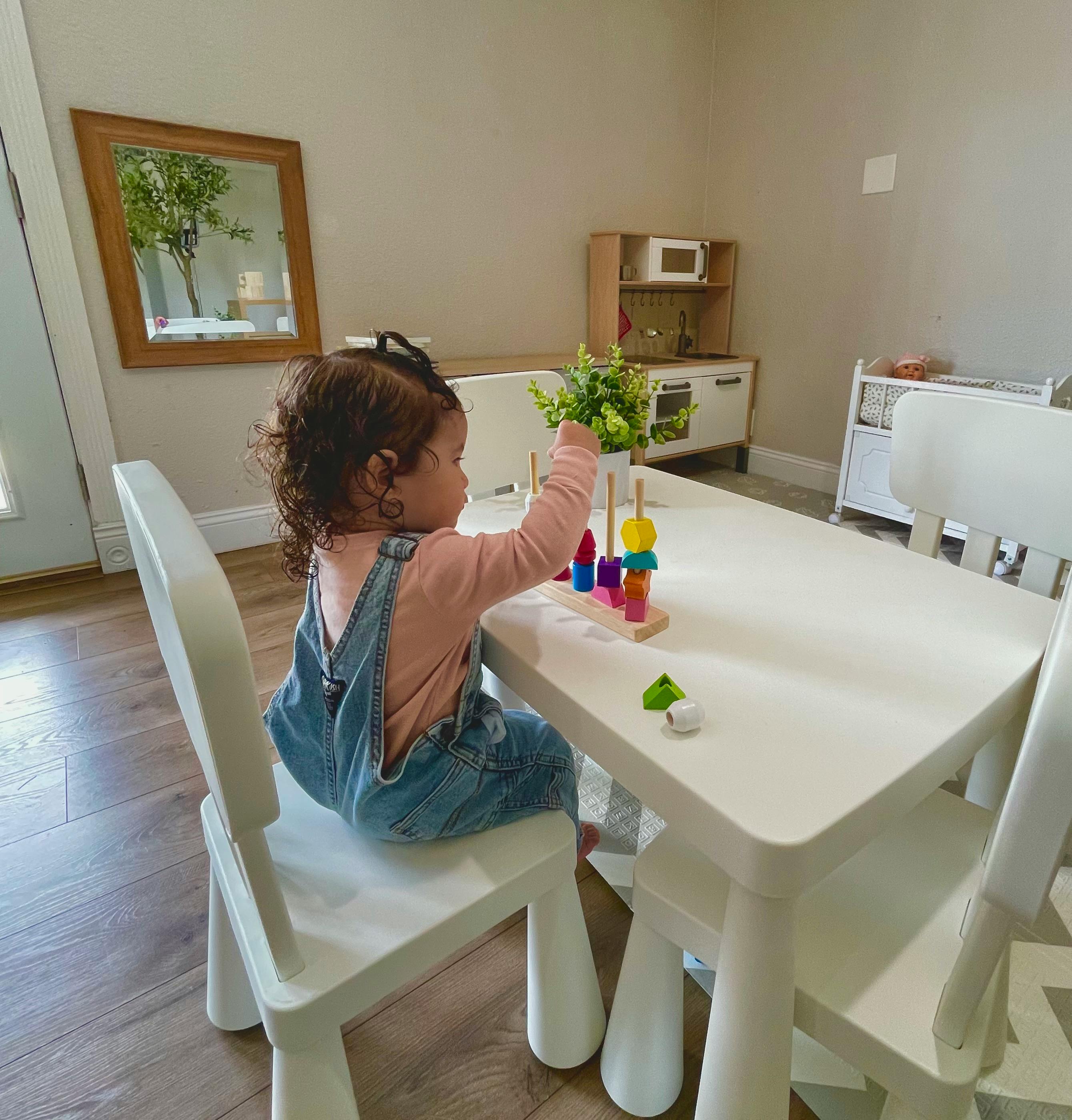 Child playing with a colorful stacking toy at a white table