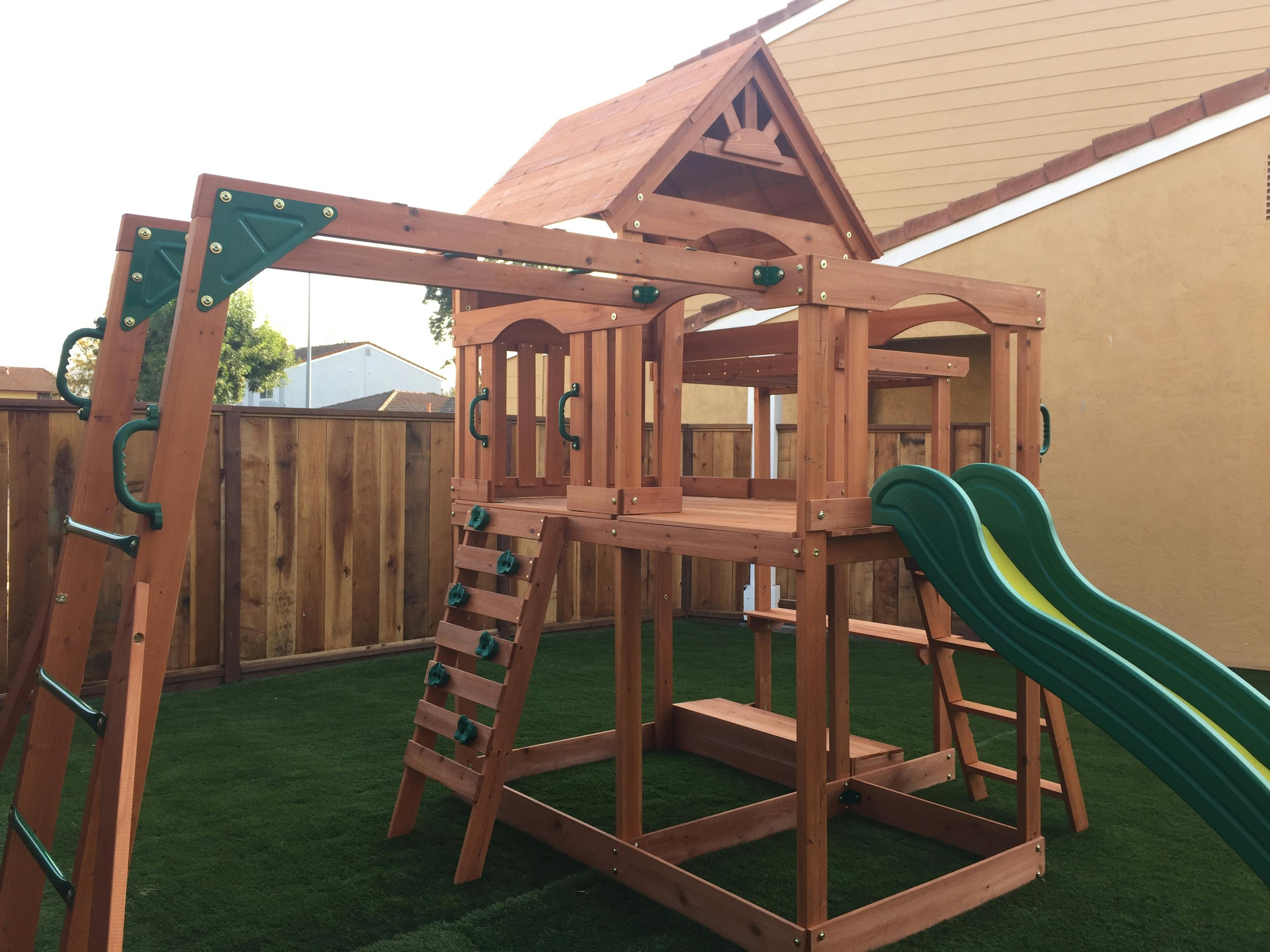 Wooden playground set with green slides and climbing wall