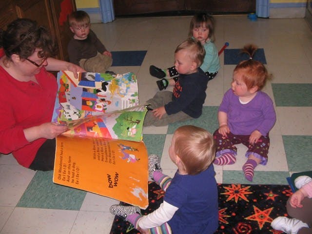 Person reading a large book to several children on the floor