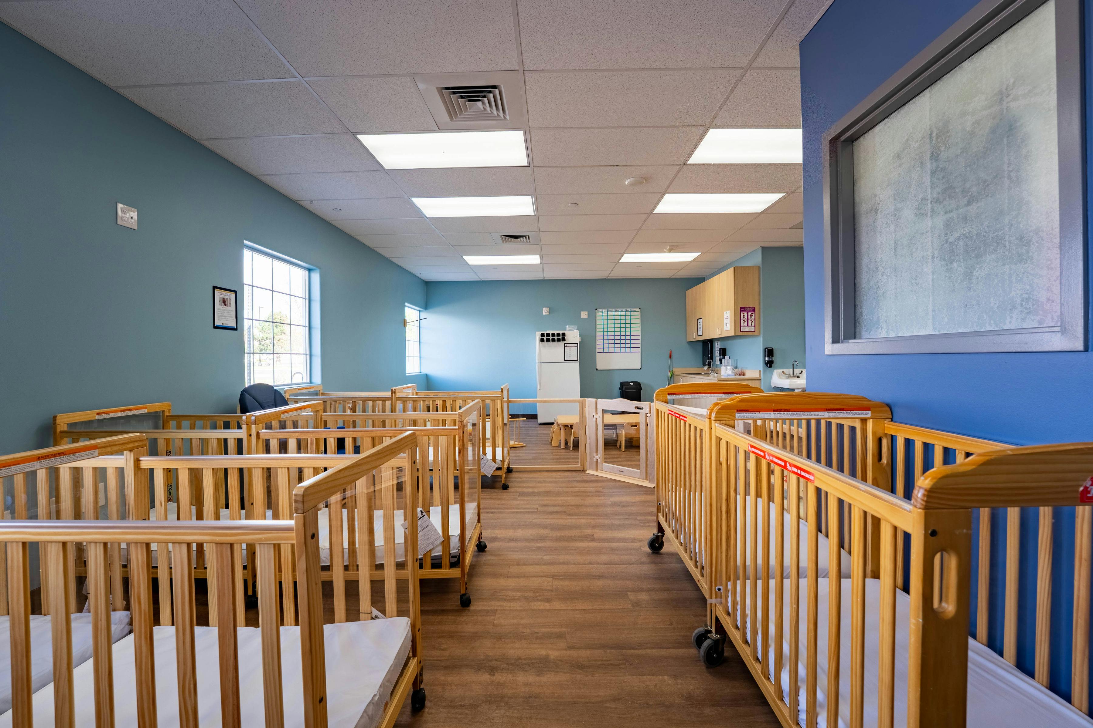 Rows of wooden cribs in a daycare room with light blue walls