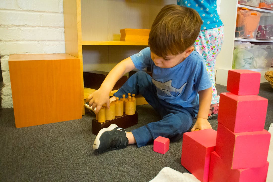 Child playing with wooden cylinders and red blocks on the floor