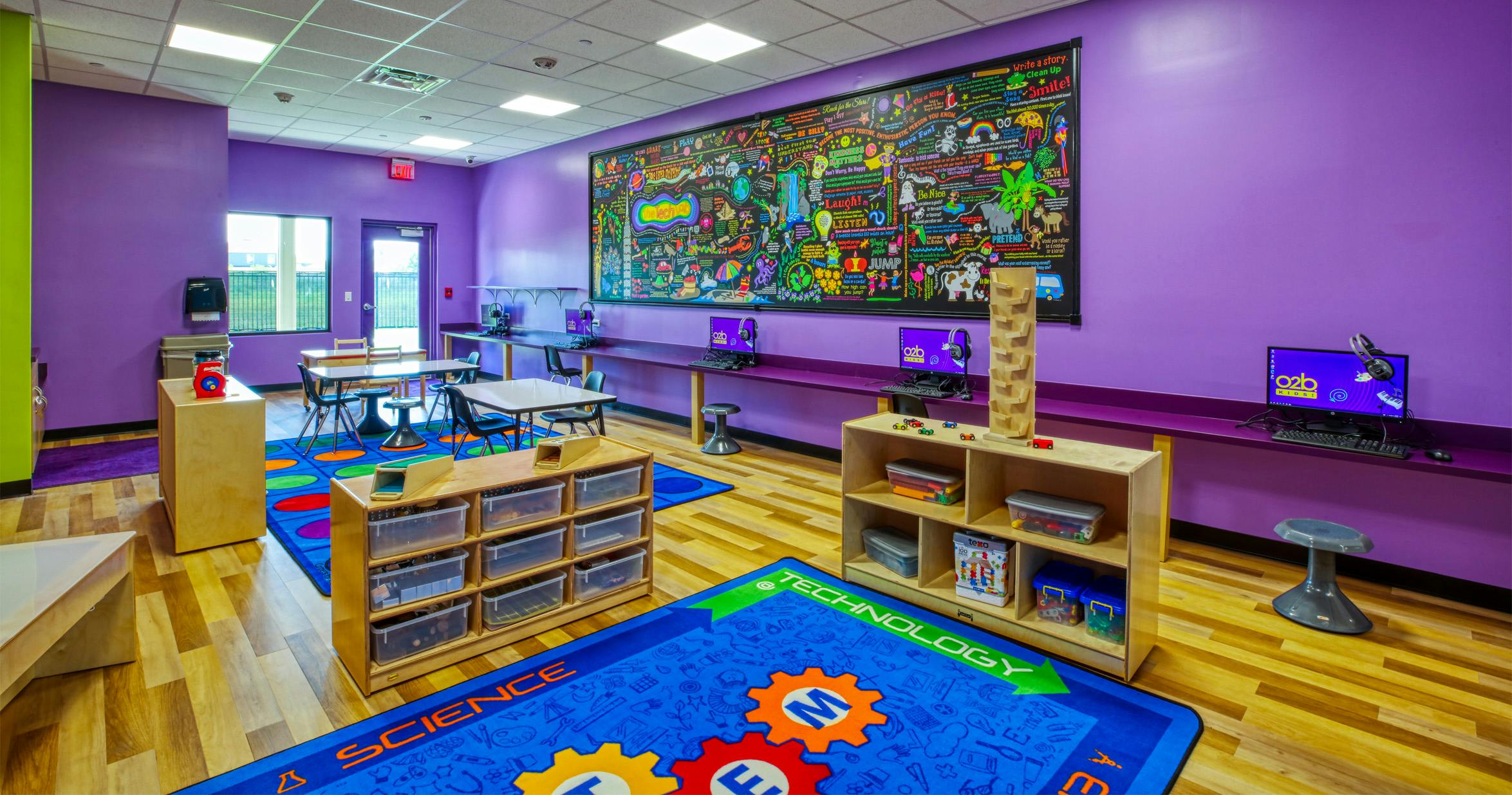 Bright purple classroom with a large colorful mural on one wall, computers, and play rugs