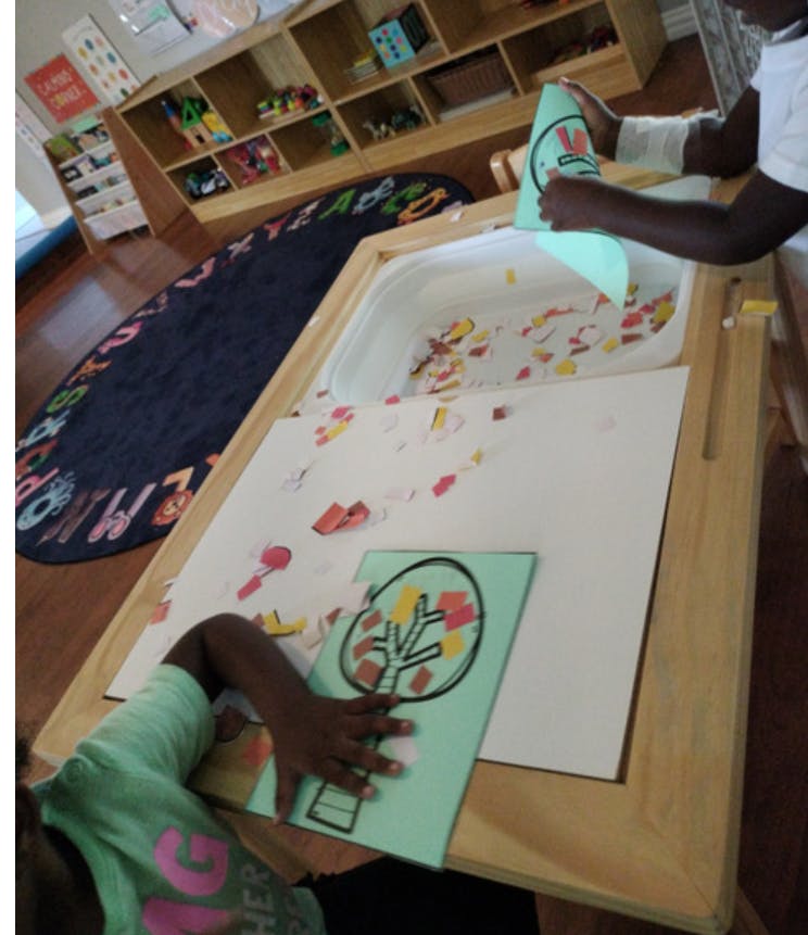 Two people doing an art project with paper cutouts and a tree drawing