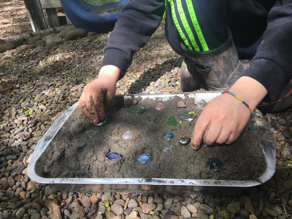 Child playing with dirt and glass gems in a tray
