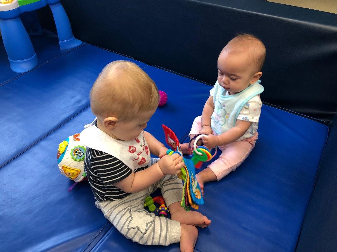 Two babies playing with toys on a blue mat