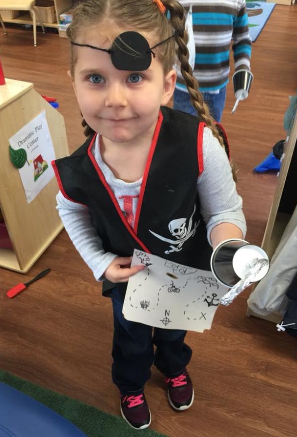 Child in pirate costume with eye patch, holding a treasure map and hook