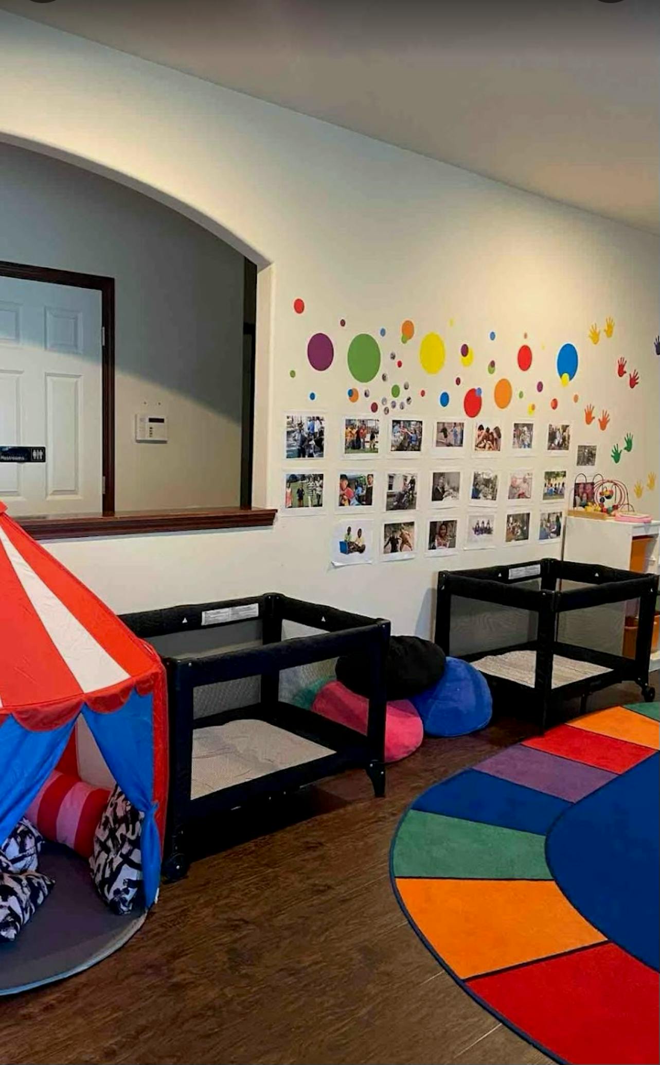 A childcare classroom with playpens, a play tent, and a colorful rug
