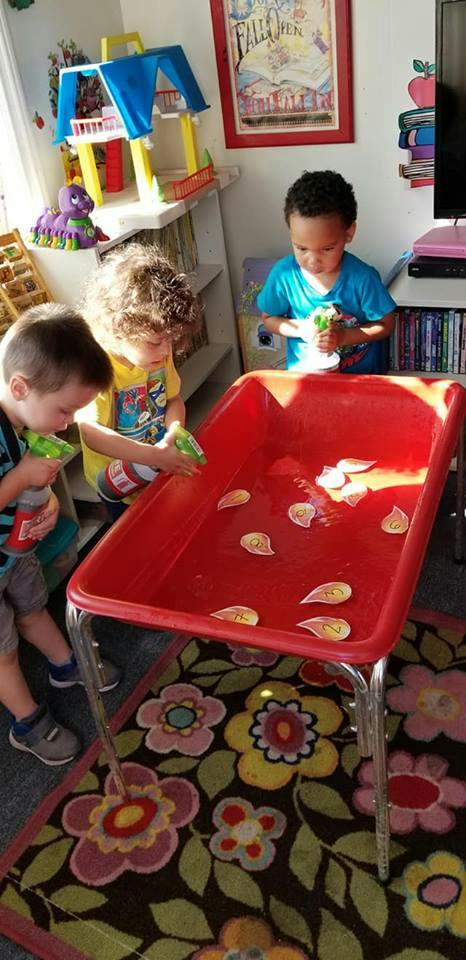 Three children spraying water into a red bin with small objects floating in it