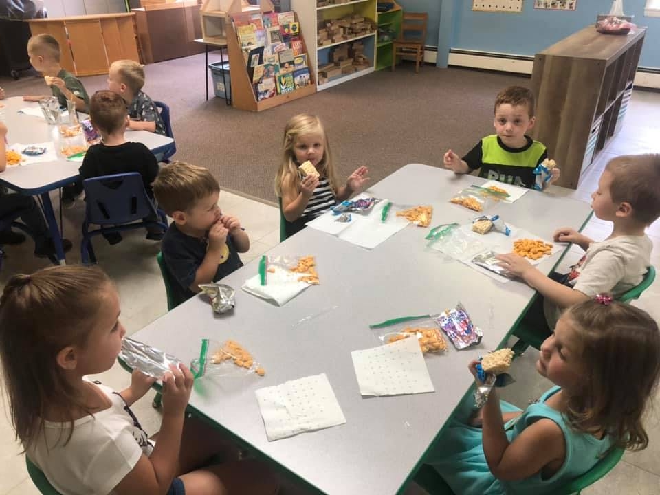 Children eating snacks at tables in a classroom