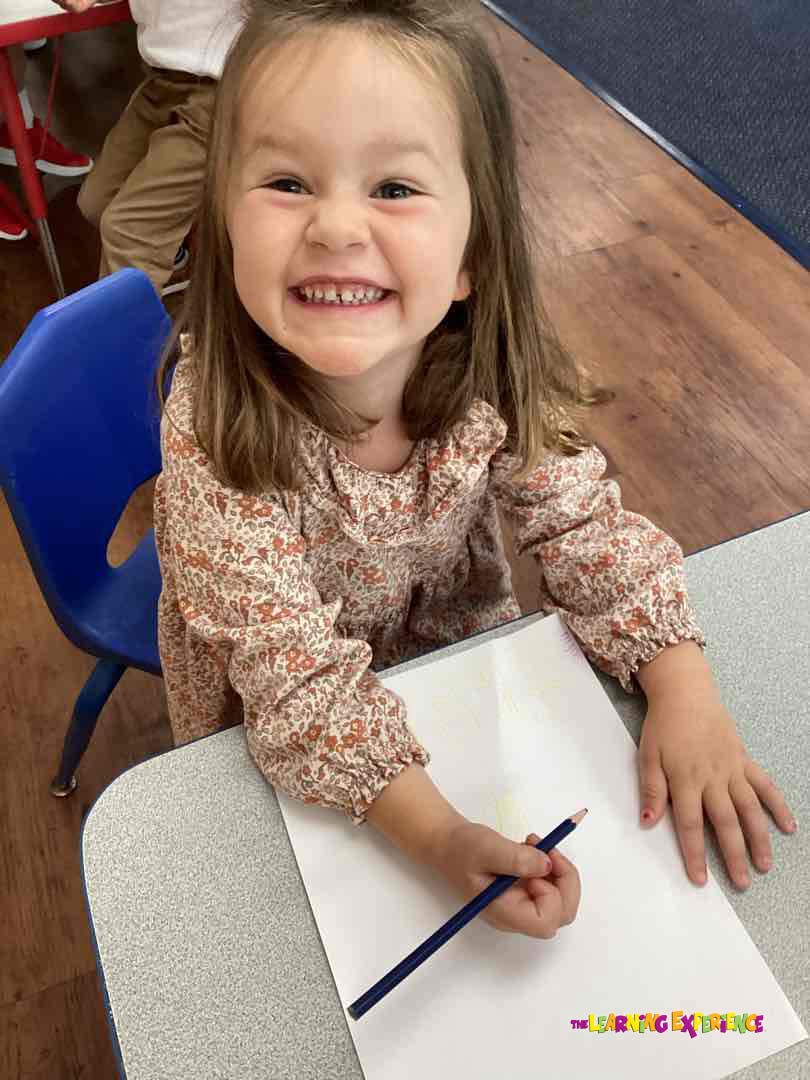Child holding a pencil over a blank sheet of paper at a desk