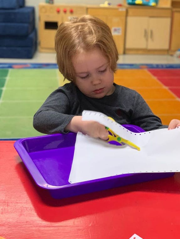 Child cutting paper with scissors in a classroom