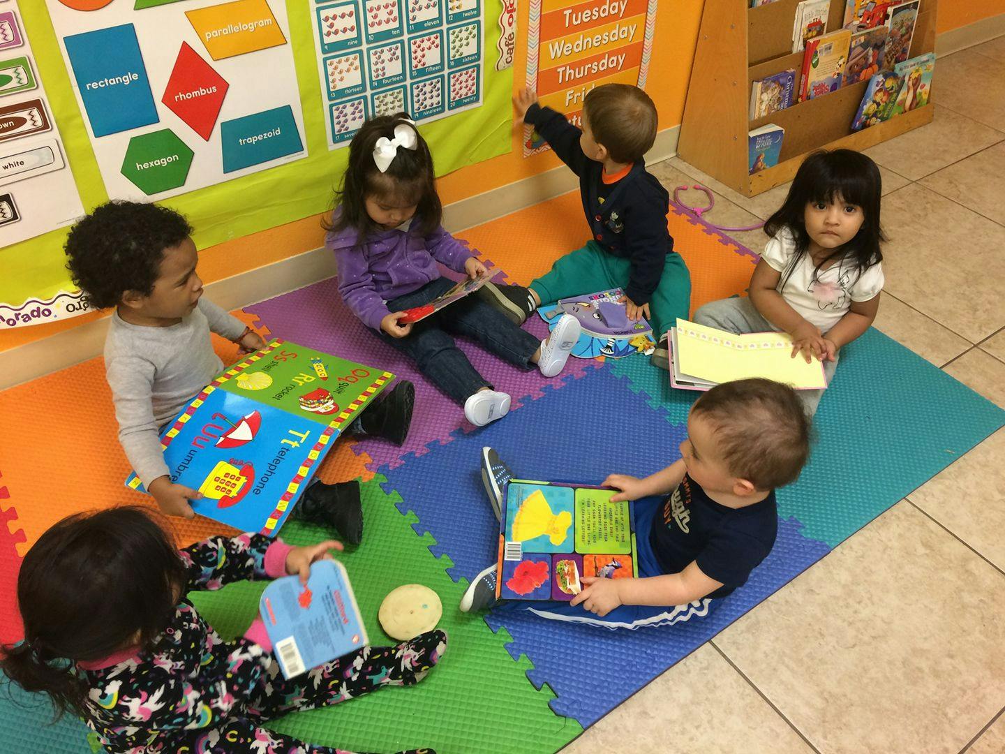 Children sitting on floor mats reading books in a classroom