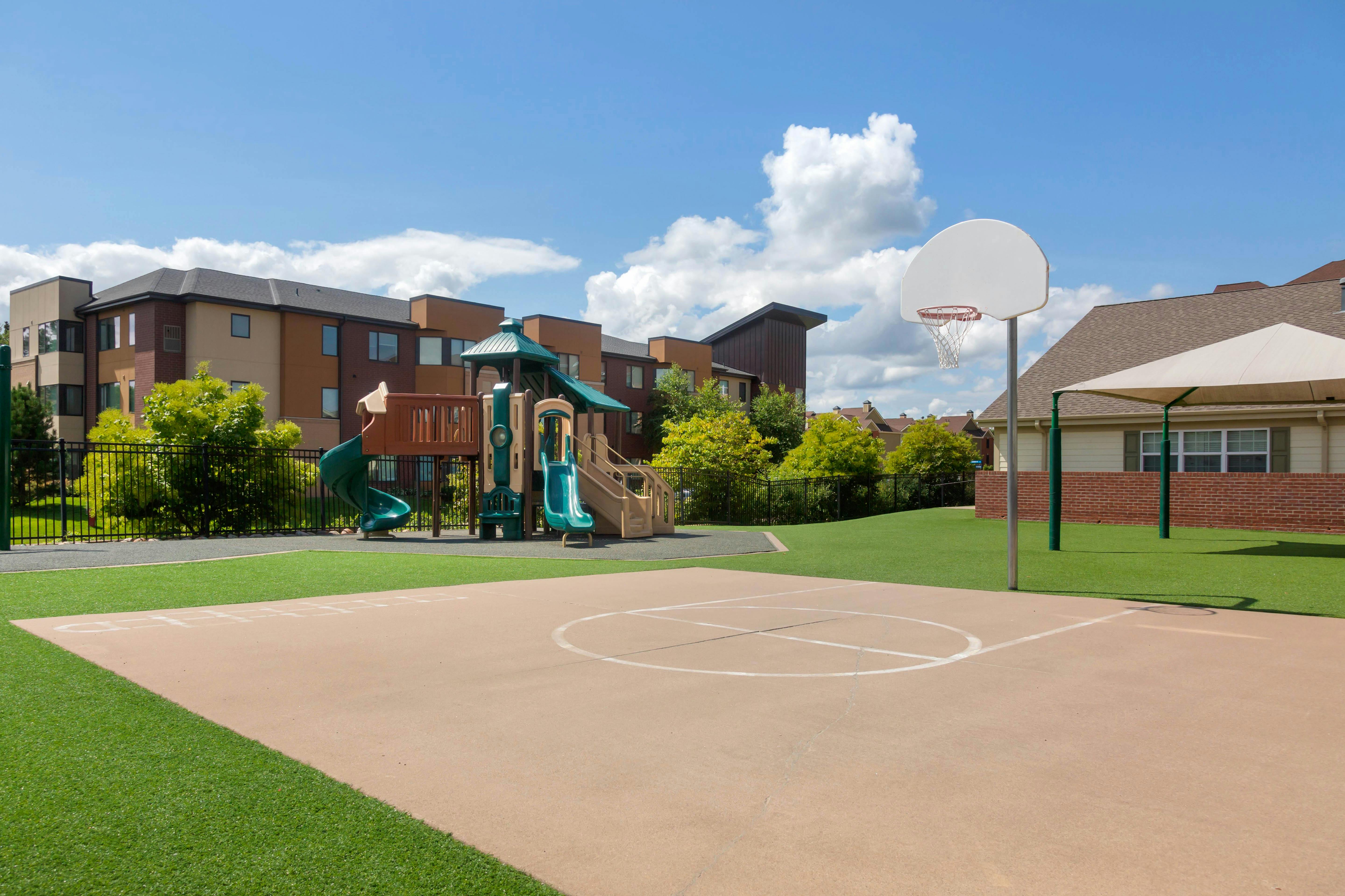 Basketball court and playground set on artificial turf with buildings in the background