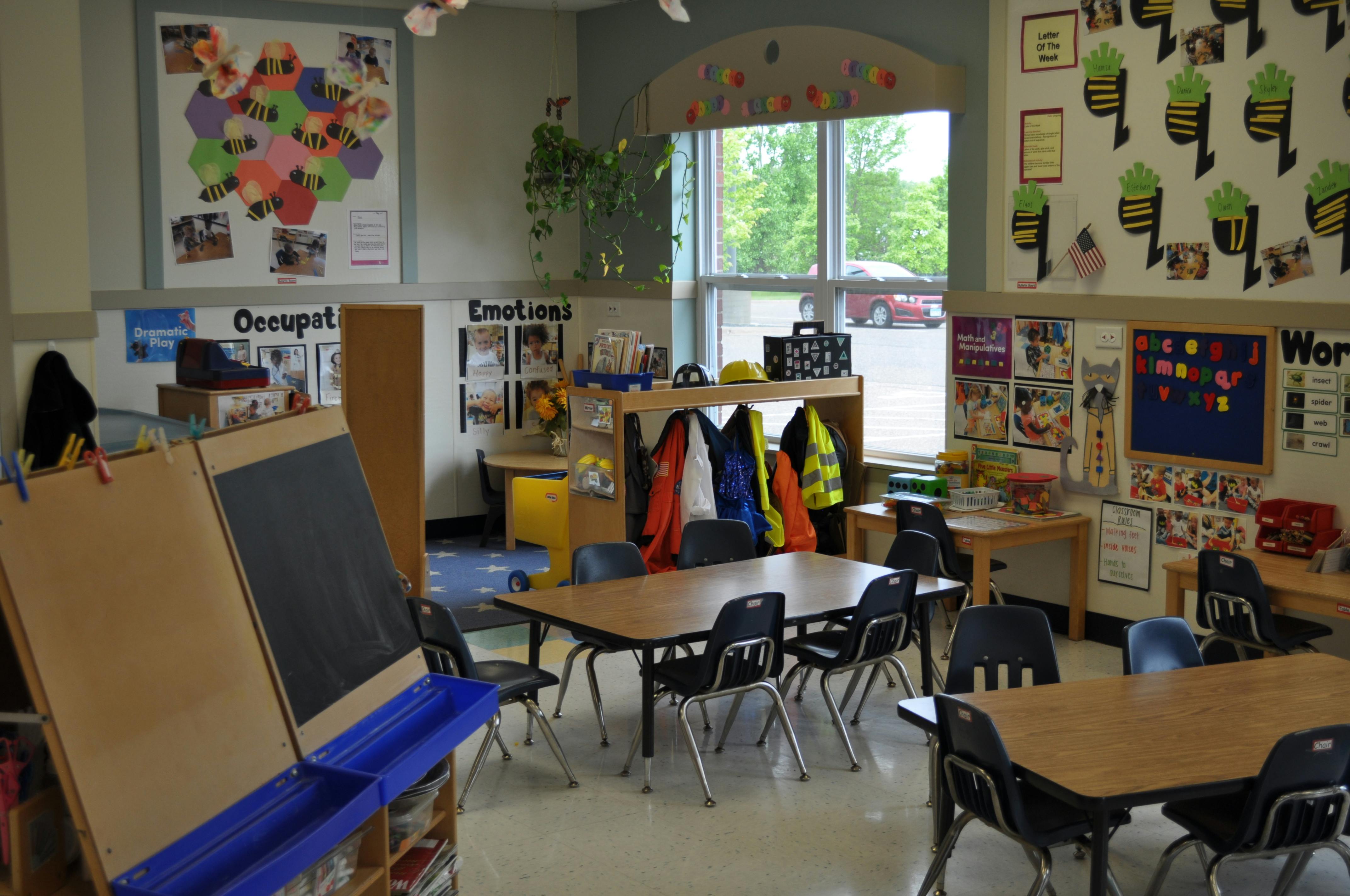 An empty classroom with small tables and chairs, educational posters on walls