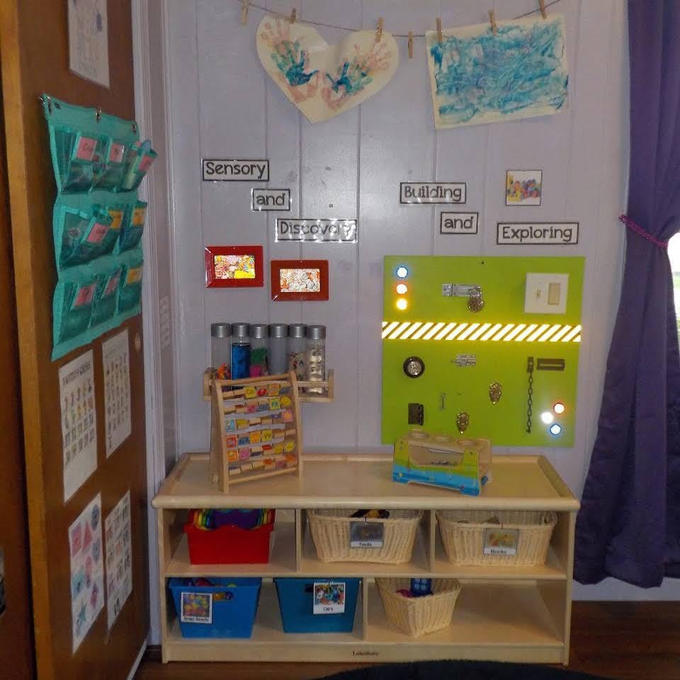 Classroom corner with a wooden shelf, storage bins, and a green activity board
