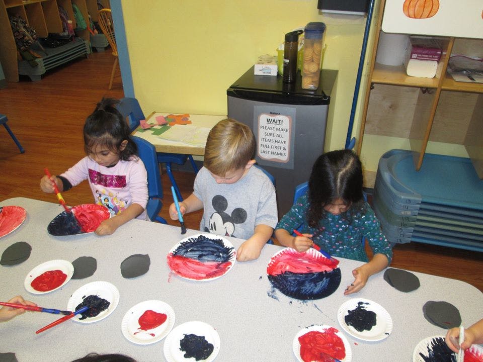 Three children painting paper plates at a table
