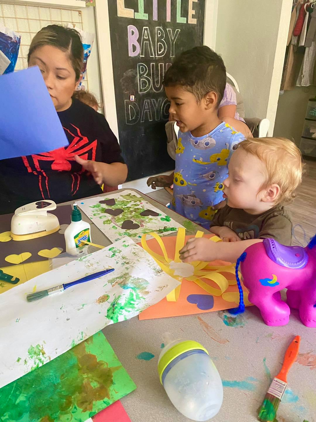 Adult and two children doing crafts at an art activity with paper, glue, and paint