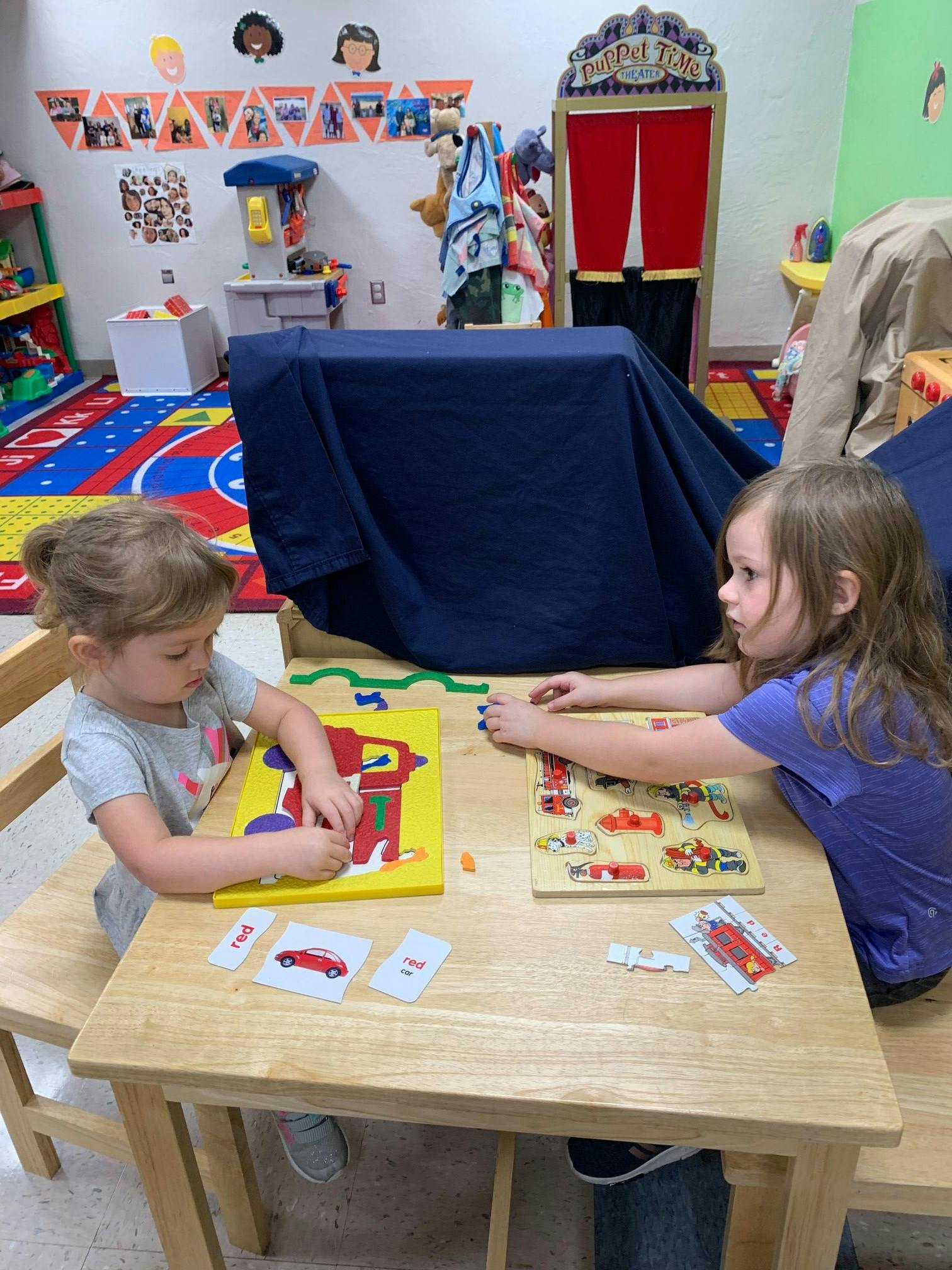 Two children playing with puzzles at a table in a classroom