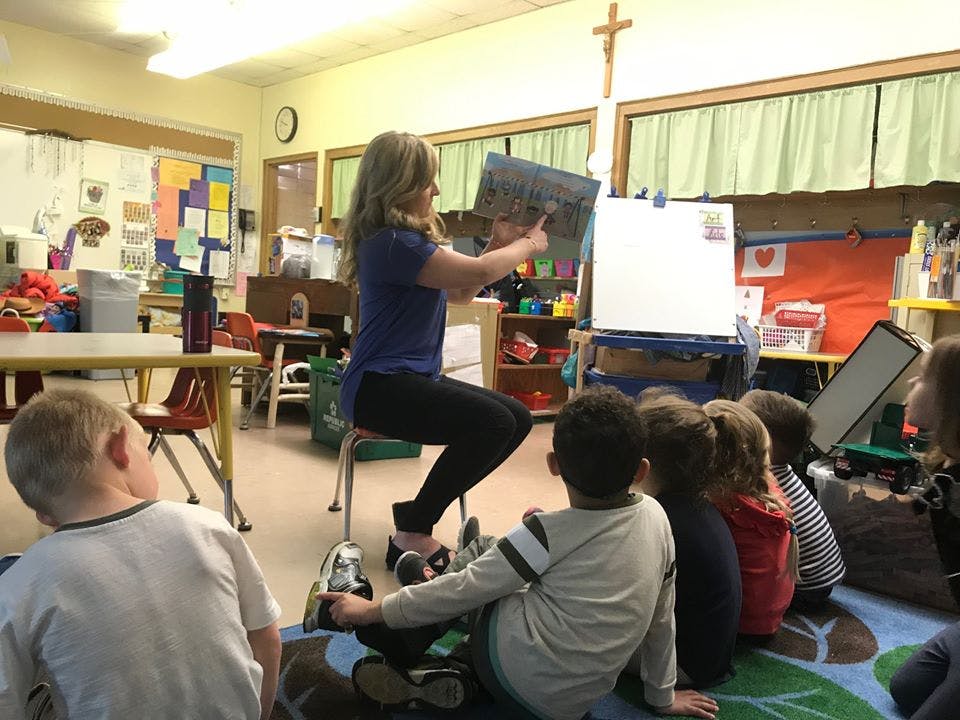 Person reading a book to a group of children in a classroom