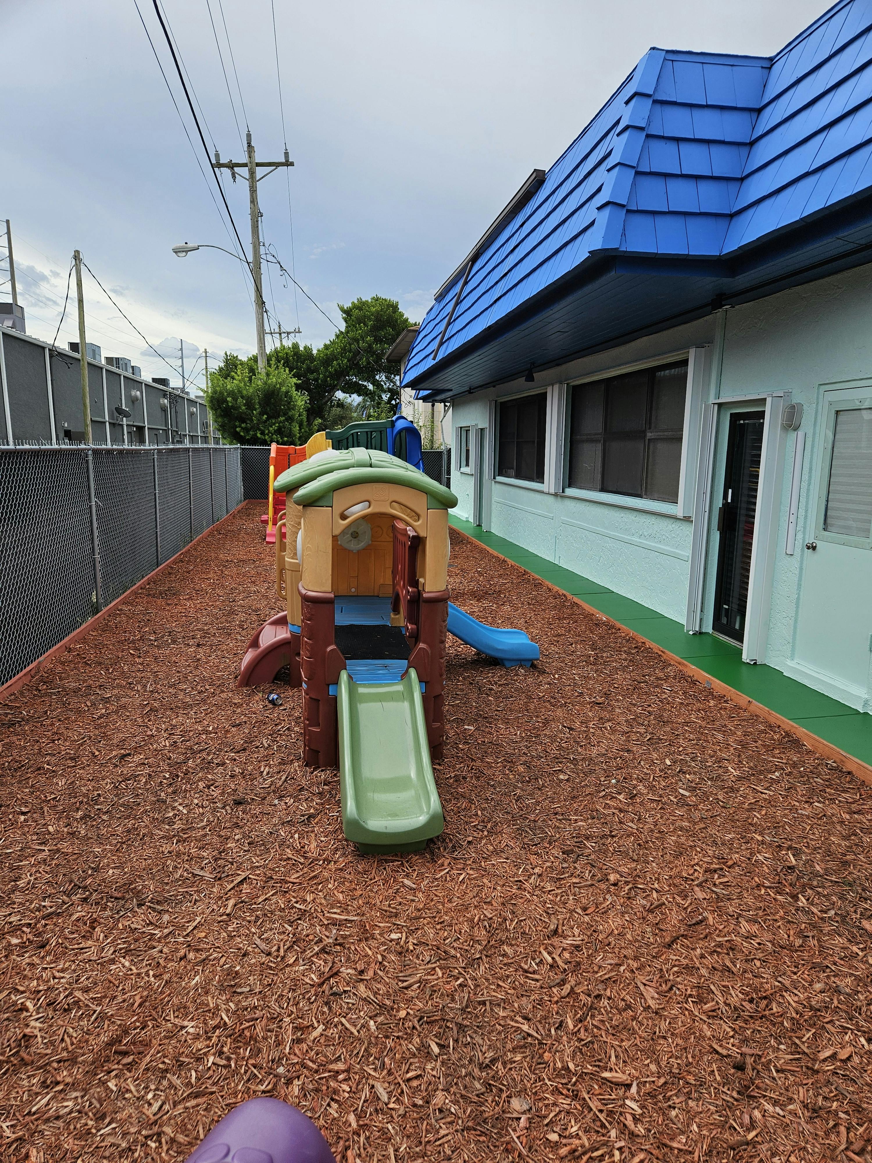 Playground with a slide and wood chips next to a building