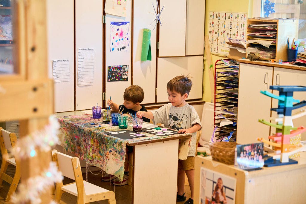 Two children painting at a table in a classroom