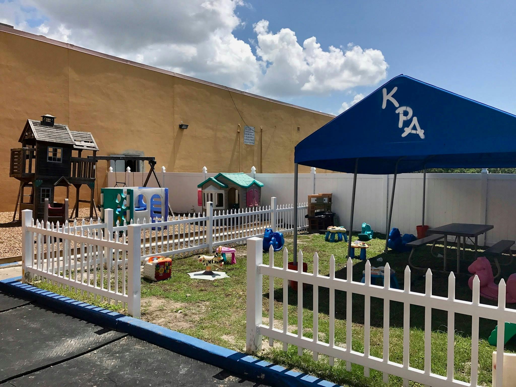Outdoor play area with a white picket fence, playhouses, and a blue tent