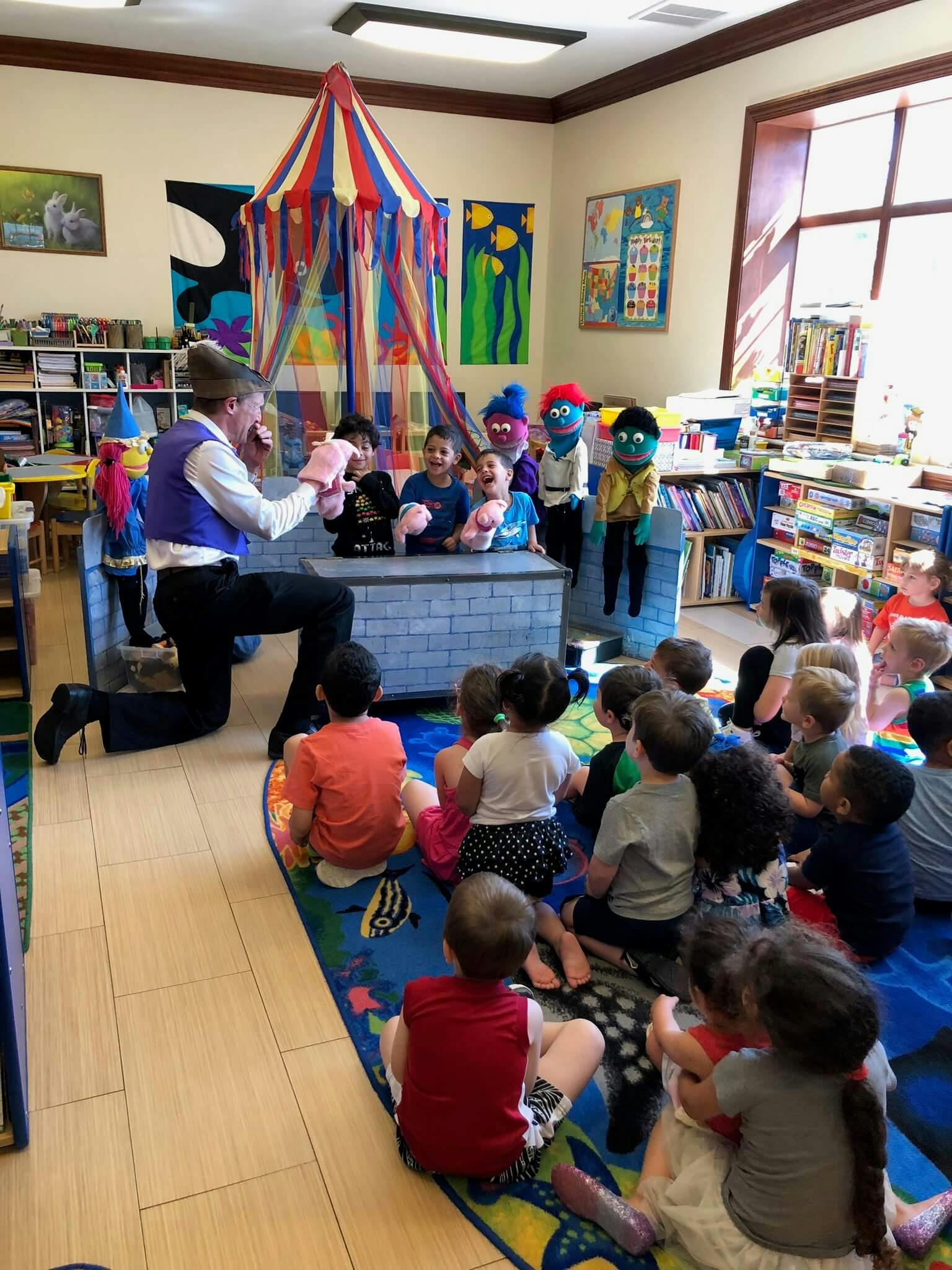 Person on one knee performing a puppet show for children in a classroom
