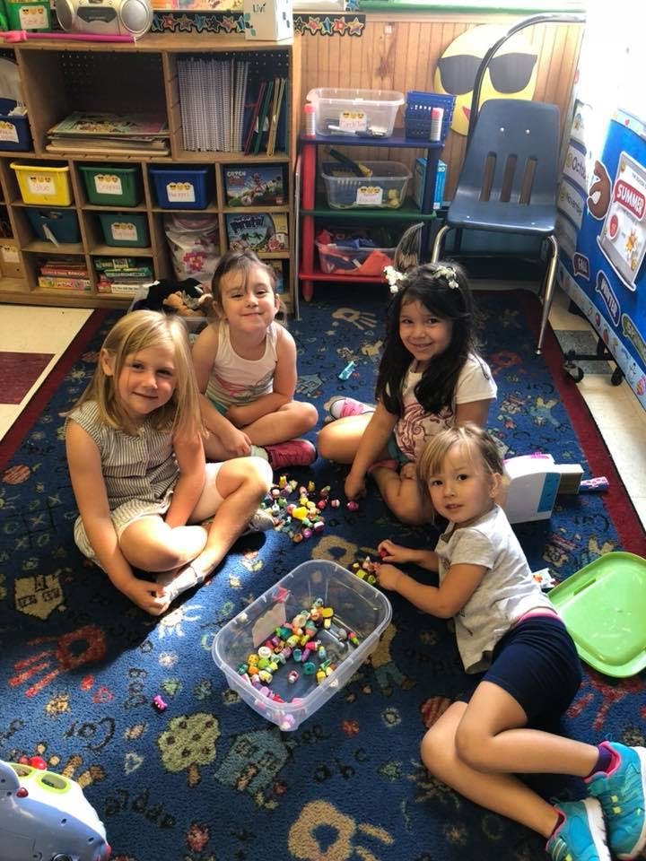 Four children playing with small colorful objects on a rug