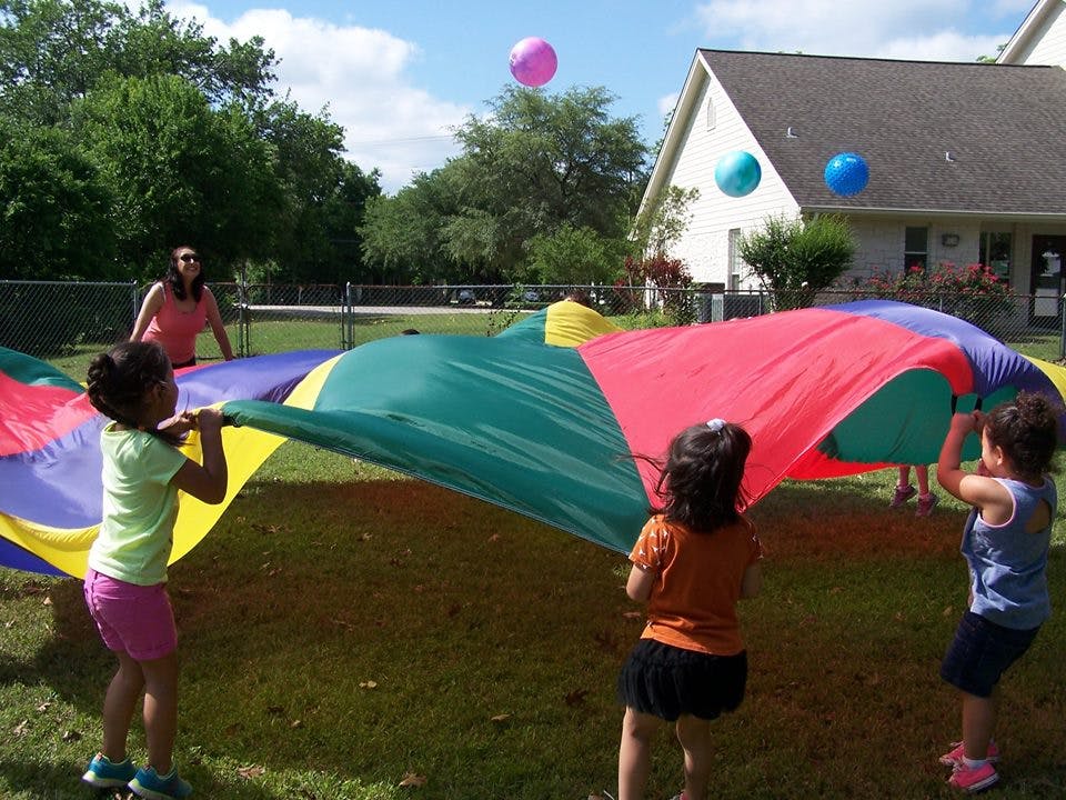 Children and an adult playing with a colorful parachute and balls outdoors