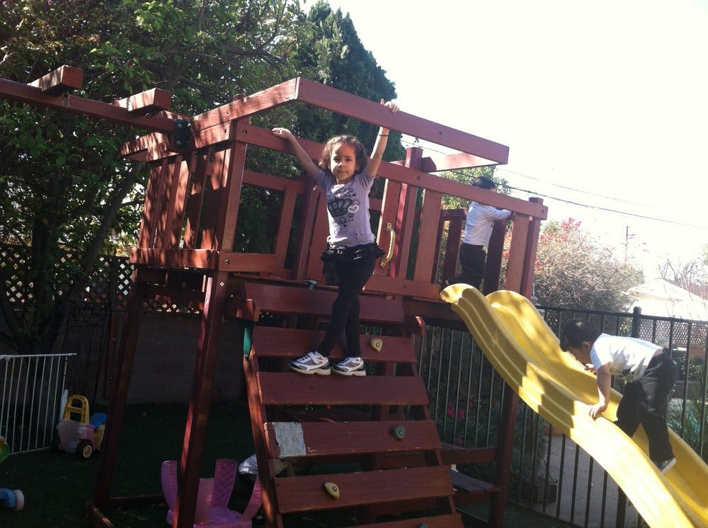 Child standing on a wooden play structure with arms raised