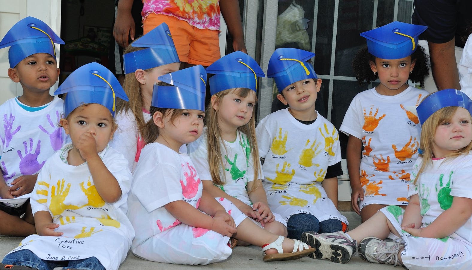 Group of children wearing blue graduation caps and handprint shirts