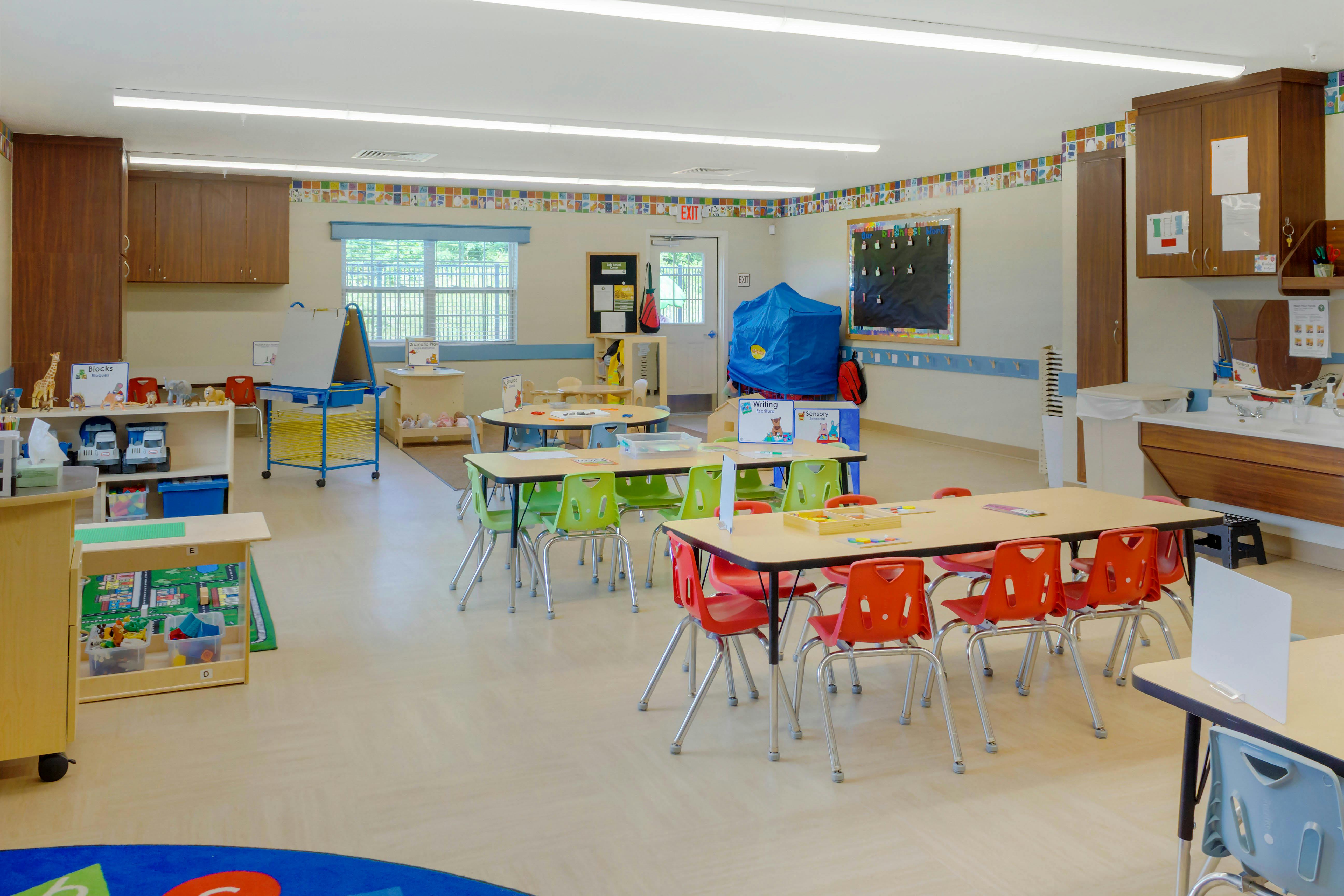 An empty early childhood classroom with multiple tables and chairs