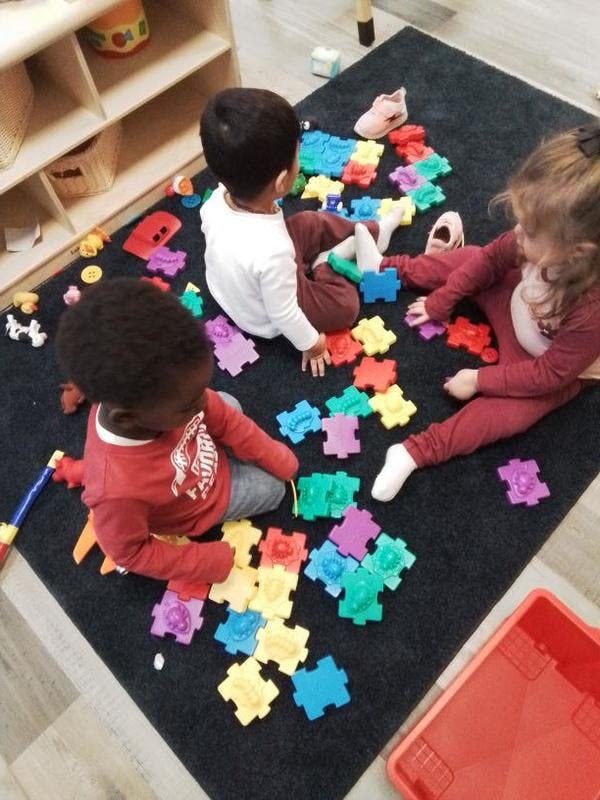 Three children playing with colorful interlocking puzzle pieces on a rug