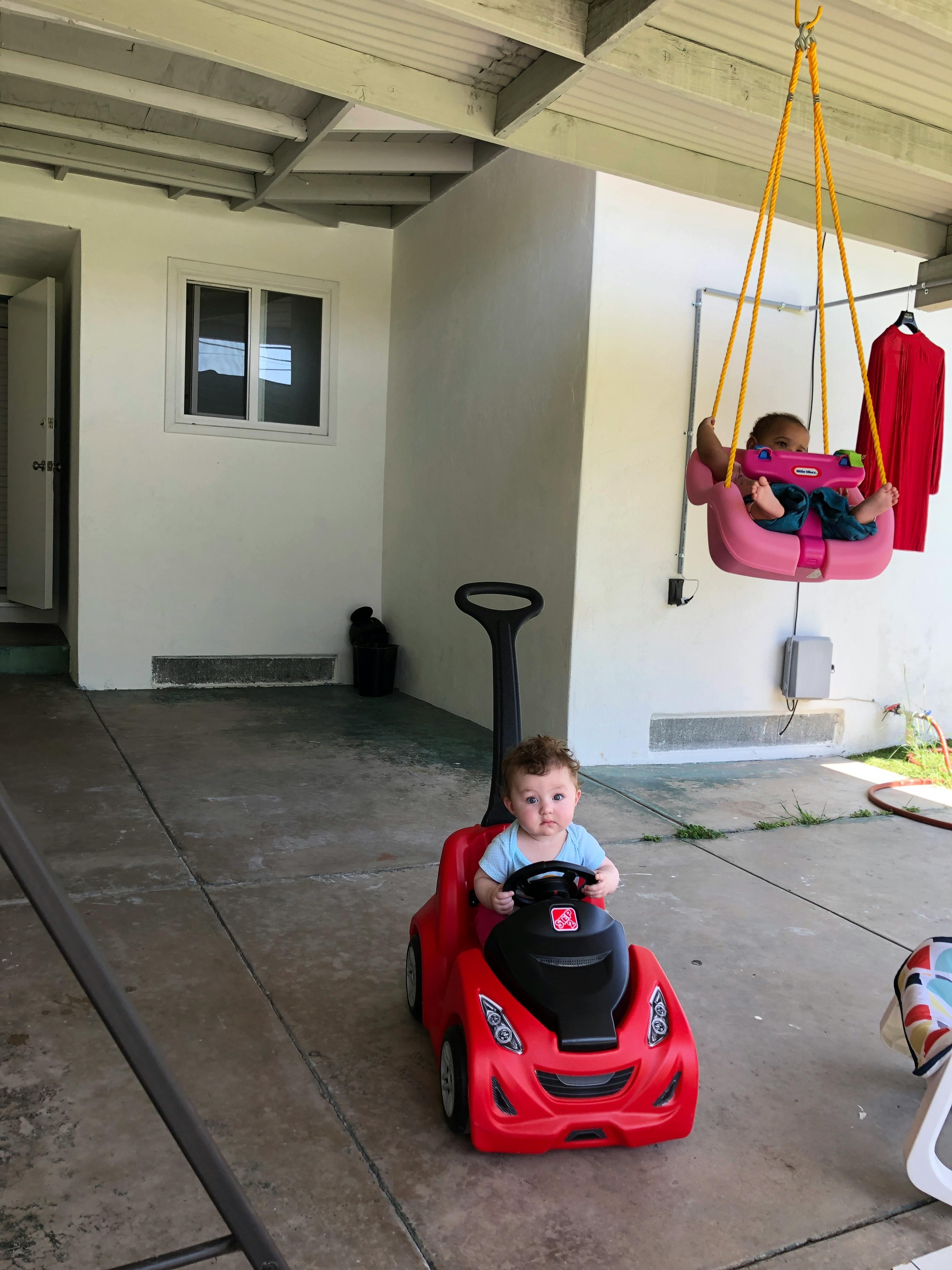 Child in a red toy car and another child in a pink swing