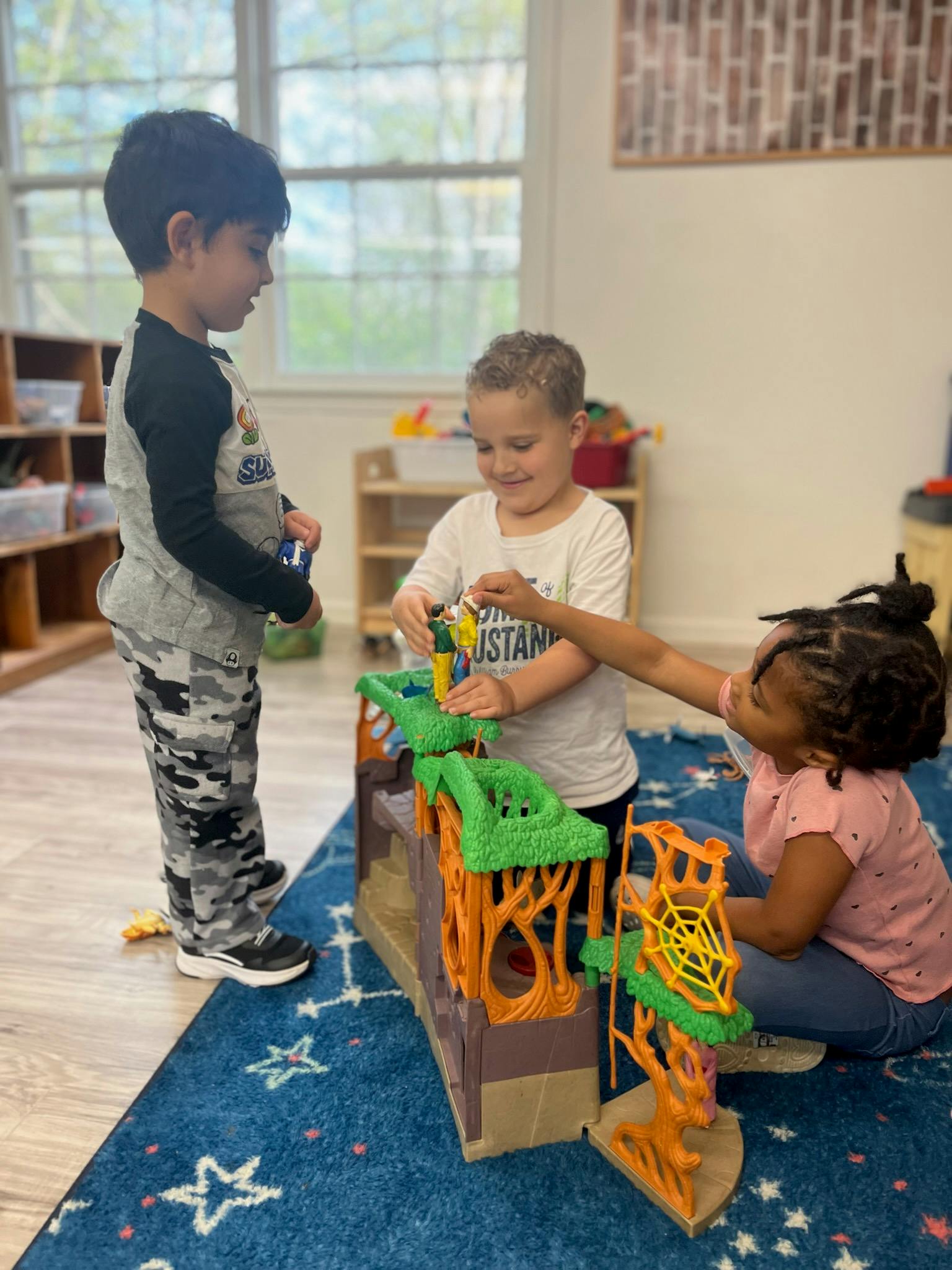Three children playing with a toy playset on a blue rug
