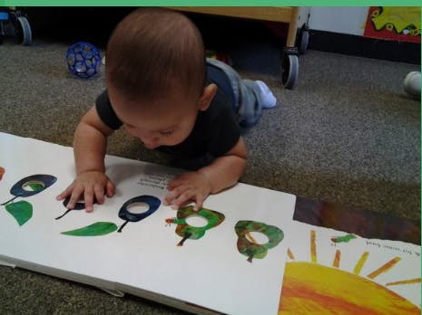 Child on floor looking at a book with colorful illustrations