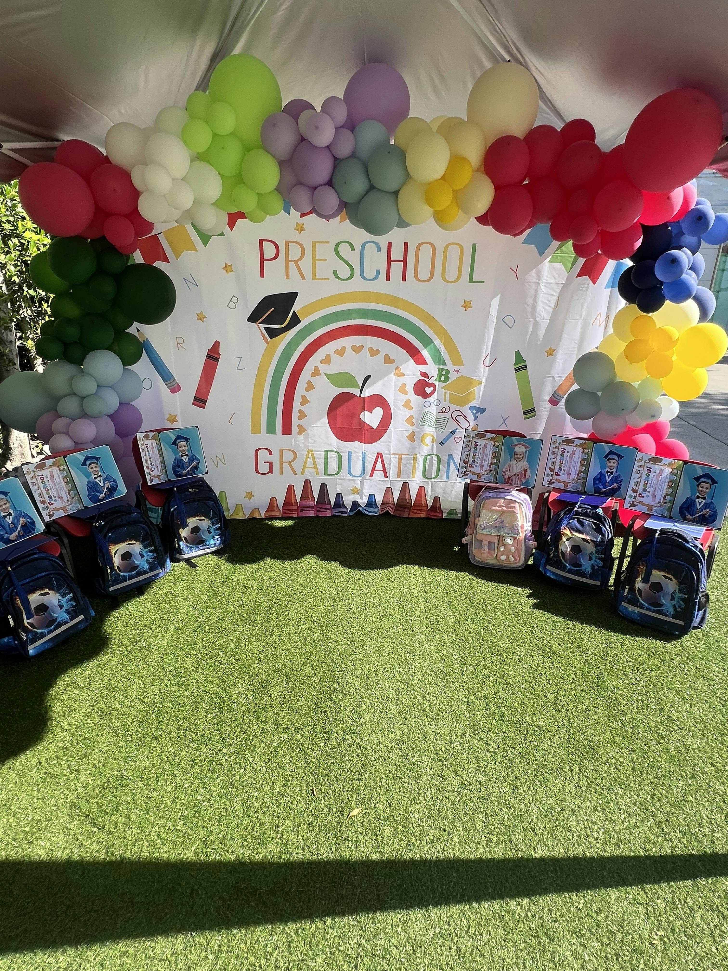 Preschool graduation banner with balloons and backpacks on artificial grass