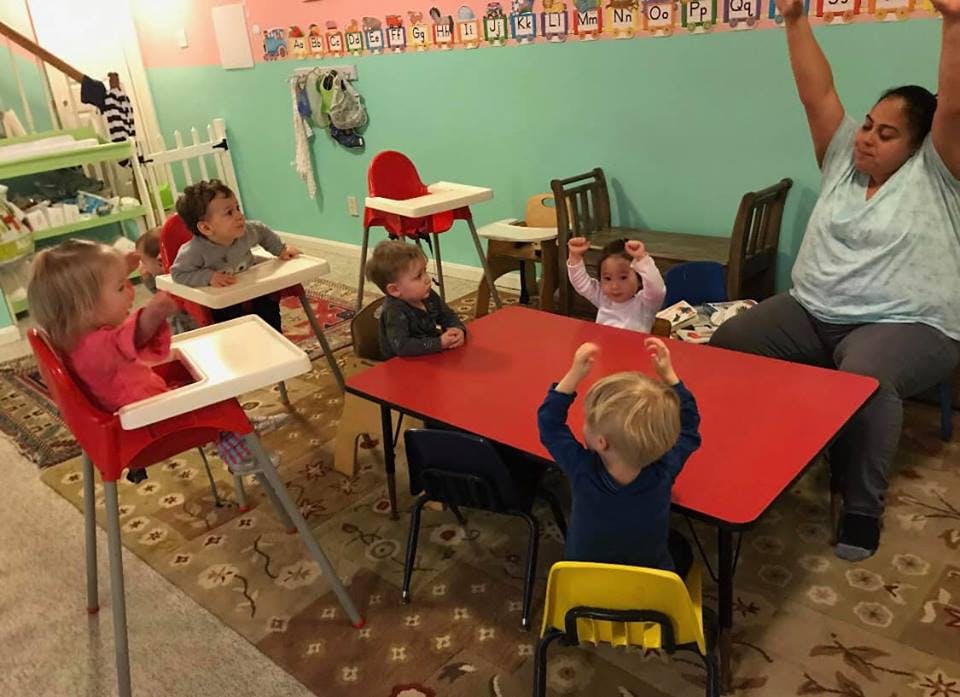 Adult and children sitting at tables with arms raised in a classroom