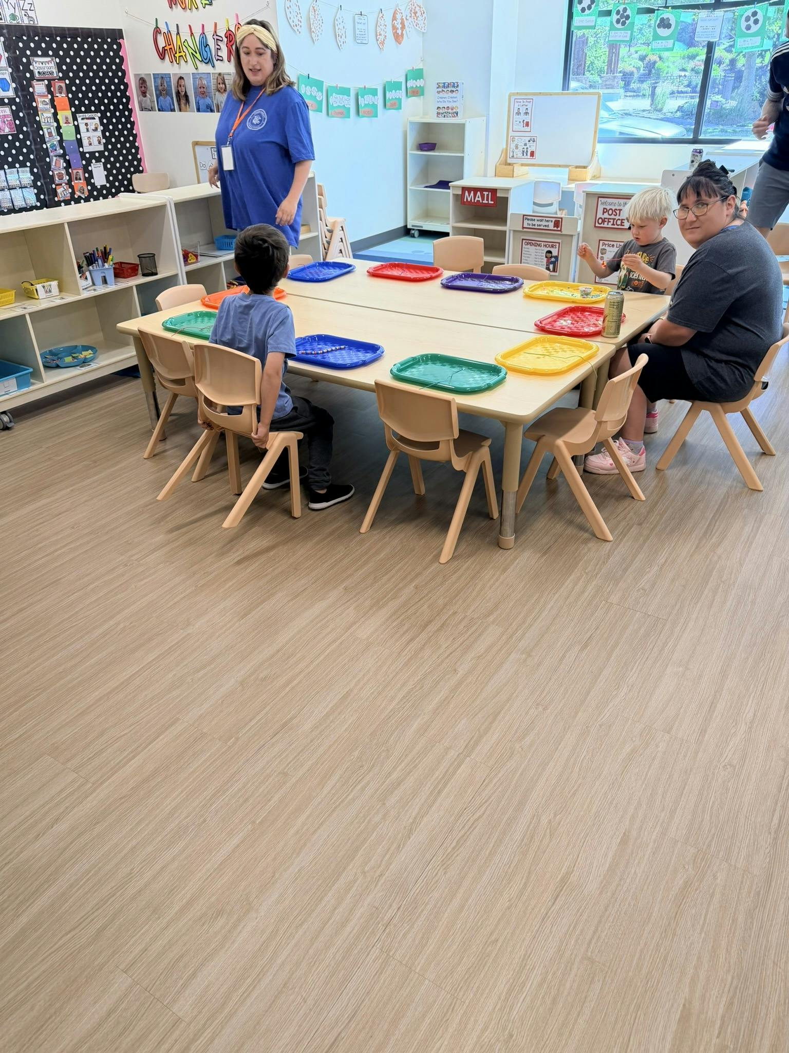 Children and adults sitting around a table with activity trays in a classroom