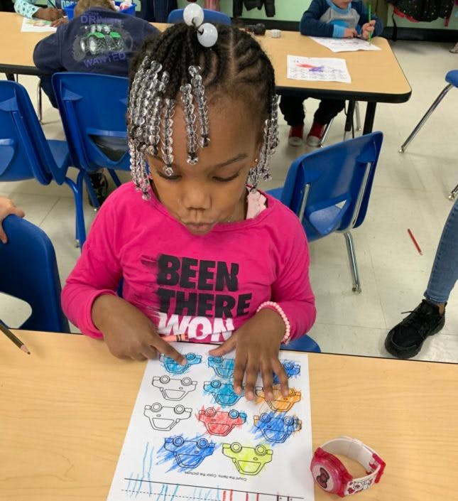 Child coloring a picture of cars at a desk