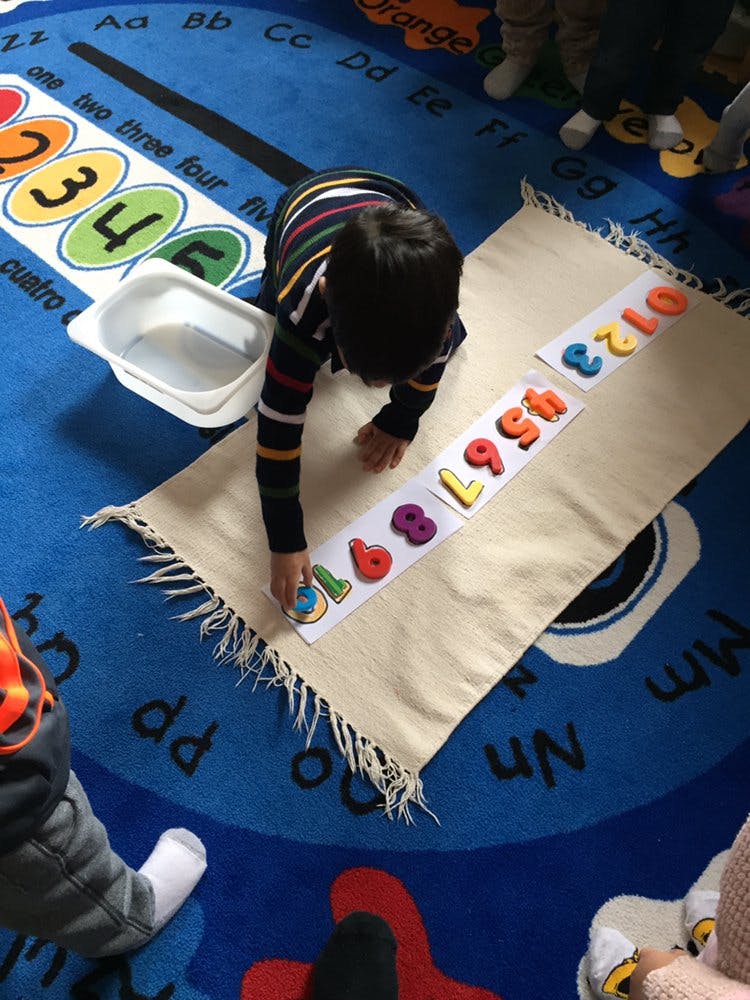 Child on a blue rug placing number cutouts on a mat