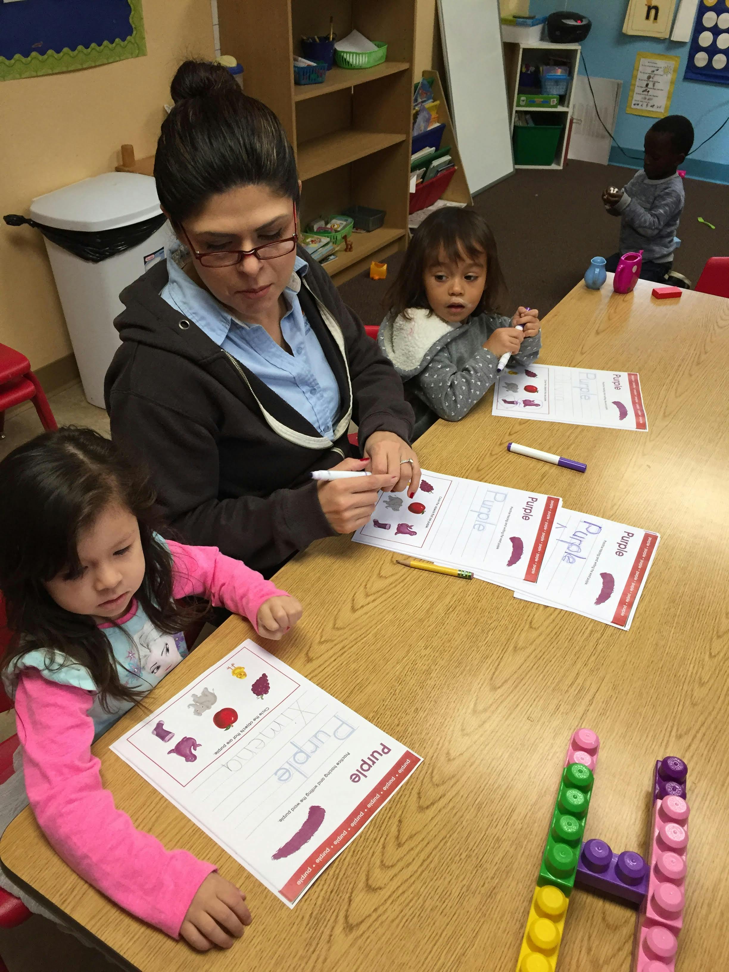 Adult and two children at a table with papers and markers